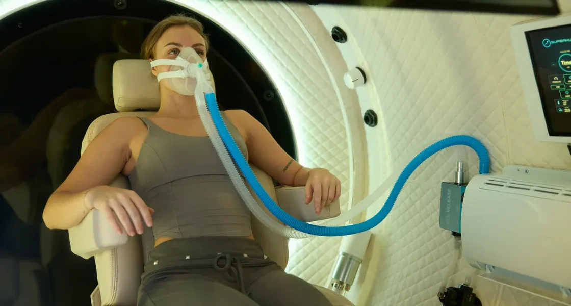 A woman reclined in the X seat, breathing through the oxygen mask on its blue hose