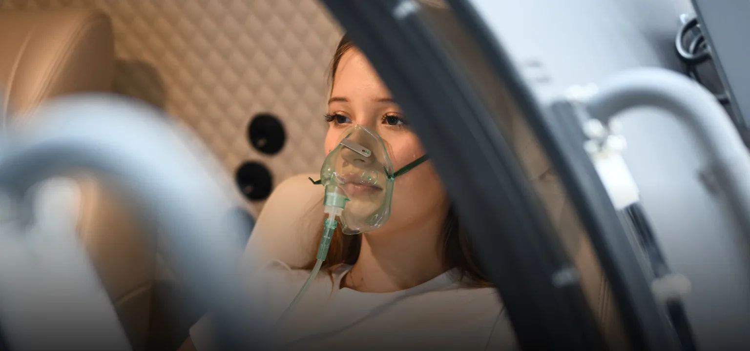 Woman wearing an oxygen mask inside a hyperbaric chamber, seen through the open chamber window